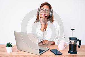 Middle age brunette hispanic woman working at the office wearing operator headset smiling looking confident at the camera with