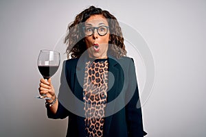 Middle age brunette woman drinking glass of red wine over isolated white background scared in shock with a surprise face, afraid