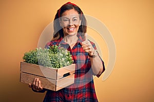 Middle age brunette woman holding wooden box garden of fresh plants happy with big smile doing ok sign, thumb up with fingers,