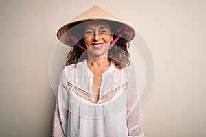Middle age brunette woman wearing asian traditional conical hat over white background with a happy and cool smile on face
