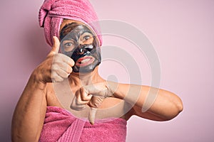 Middle age brunette woman wearing beauty black face mask over isolated pink background Doing thumbs up and down, disagreement and