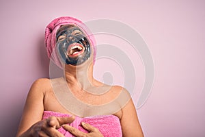 Middle age brunette woman wearing beauty black face mask over isolated pink background laughing at you, pointing finger to the