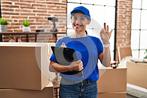 Middle age brunette woman wearing delivery uniform at house moving doing ok sign with fingers, smiling friendly gesturing