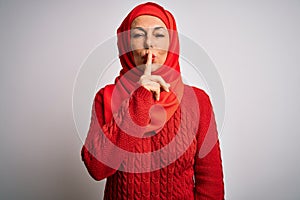 Middle age brunette woman wearing muslim traditional hijab over isolated white background asking to be quiet with finger on lips