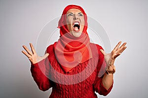 Middle age brunette woman wearing muslim traditional hijab over isolated white background crazy and mad shouting and yelling with