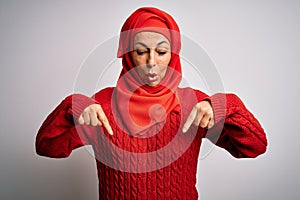 Middle age brunette woman wearing muslim traditional hijab over isolated white background Pointing down with fingers showing