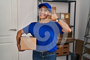 Middle age brunette woman working wearing delivery uniform and cap smiling doing phone gesture with hand and fingers like talking