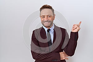 Middle age business man with beard wearing suit and tie with a big smile on face, pointing with hand finger to the side looking at