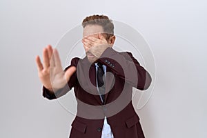 Middle age business man with beard wearing suit and tie covering eyes with hands and doing stop gesture with sad and fear