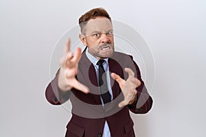 Middle age business man with beard wearing suit and tie shouting frustrated with rage, hands trying to strangle, yelling mad