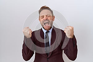 Middle age business man with beard wearing suit and tie very happy and excited doing winner gesture with arms raised, smiling and