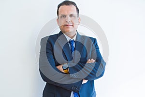 Middle age business man looking natural and relaxed with crossed arms over white wall background
