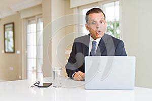 Middle age business man working with computer laptop afraid and shocked with surprise expression, fear and excited face