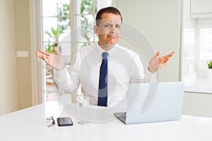 Middle age business man working with computer laptop clueless and confused expression with arms and hands raised