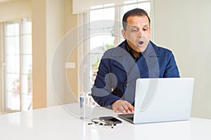 Middle age business man working using laptop afraid and shocked with surprise expression, fear and excited face