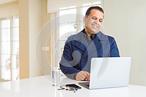 Middle age business man working using laptop looking away to side with smile on face, natural expression