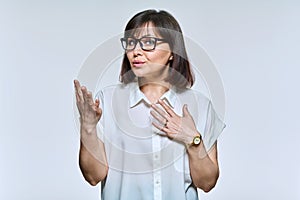 Middle age business woman in glasses talking, looking at camera, on light background