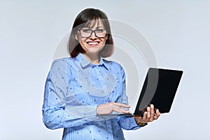 Middle age business woman using laptop, looking at camera on light background