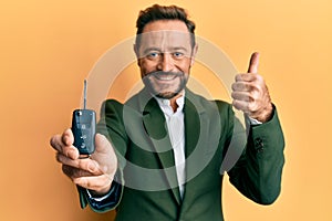 Middle age businessman holding key of new car smiling happy and positive, thumb up doing excellent and approval sign