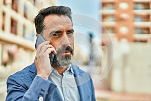 Middle age businessman with serious expresison talking on the smartphone at the city