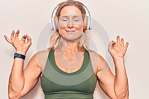 Middle age caucasian blonde woman listening to music using headphones relax and smiling with eyes closed doing meditation gesture