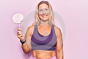 Middle age caucasian blonde woman wearing sportswear holding sugar candy looking positive and happy standing and smiling with a