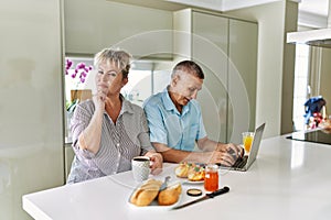 Middle age caucasian couple eating breakfast at home using laptop serious face thinking about question with hand on chin,