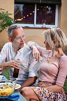 Middle age caucasian couple talk during barbecue garden dinner party outdoors.