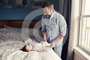 Middle age Caucasian father changing diaper clothes for newborn baby daughter son. Man parent taking care of a child at home.