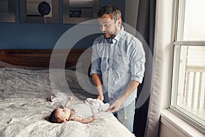 Middle age Caucasian father changing diaper clothes for newborn baby daughter son. Man parent taking care of a child at home.