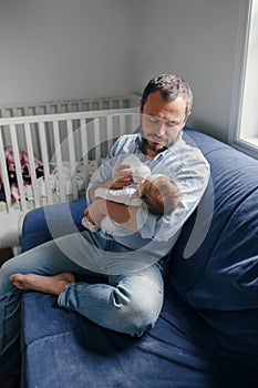 Middle age Caucasian father feeding newborn baby from bottle milk. Man parent holding rocking child on hands arms. Authentic