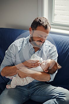 Middle age Caucasian father feeding newborn baby from bottle with milk. Man parent holding rocking child on his hands. Authentic