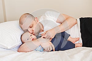 middle age Caucasian father in white t-shirt lying in bed with newborn baby son