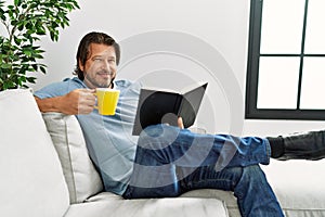 Middle age caucasian man drinking coffee reading book at home