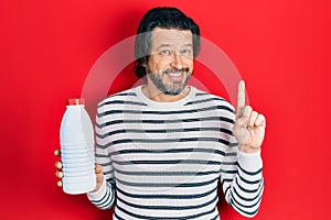 Middle age caucasian man holding liter bottle of milk smiling with an idea or question pointing finger with happy face, number one