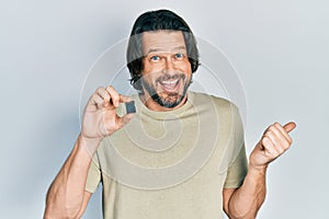 Middle age caucasian man holding sdxc card pointing thumb up to the side smiling happy with open mouth