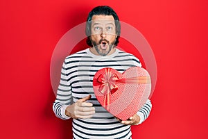 Middle age caucasian man holding valentine gift scared and amazed with open mouth for surprise, disbelief face