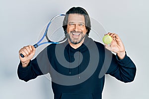 Middle age caucasian man playing tennis holding racket and ball smiling and laughing hard out loud because funny crazy joke