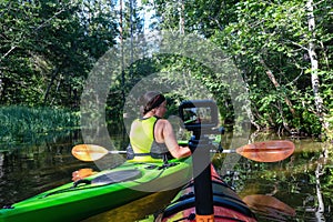 Middle age Caucasian Scandinavian women kayaking in small river in forest, one kayak with action camera collides another. Green