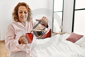 Middle age caucasian woman drinking coffee standing at bedroom