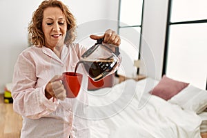 Middle age caucasian woman drinking coffee standing at bedroom