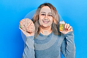 Middle age caucasian woman holding brain and pills as mental health concept smiling with a happy and cool smile on face