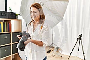 Middle age caucasian woman photographer smiling confident holding professional camera at photograph studio