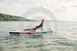 Middle age Caucasian woman practising yoga on paddle sup surfboard at sunset.