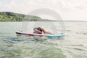 Middle age Caucasian woman practising yoga on paddle sup surfboard at sunset.