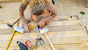 Middle age caucasian woman repairing and building furnitures using recycled wood from cargo pallets outdoor - hardware and all