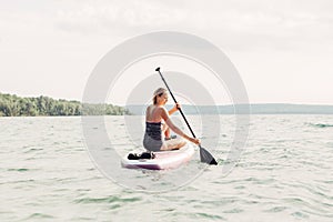 Middle age Caucasian woman sitting riding on paddle sup surfboard at sunset.
