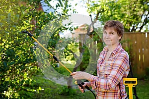 Middle age caucasian woman sprays trees against pests, vermin or diseases plants