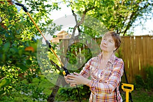 Middle age caucasian woman sprays trees against pests, vermin or diseases plants. Seasonal working in garden