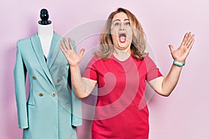 Middle age caucasian woman standing by manikin crazy and mad shouting and yelling with aggressive expression and arms raised